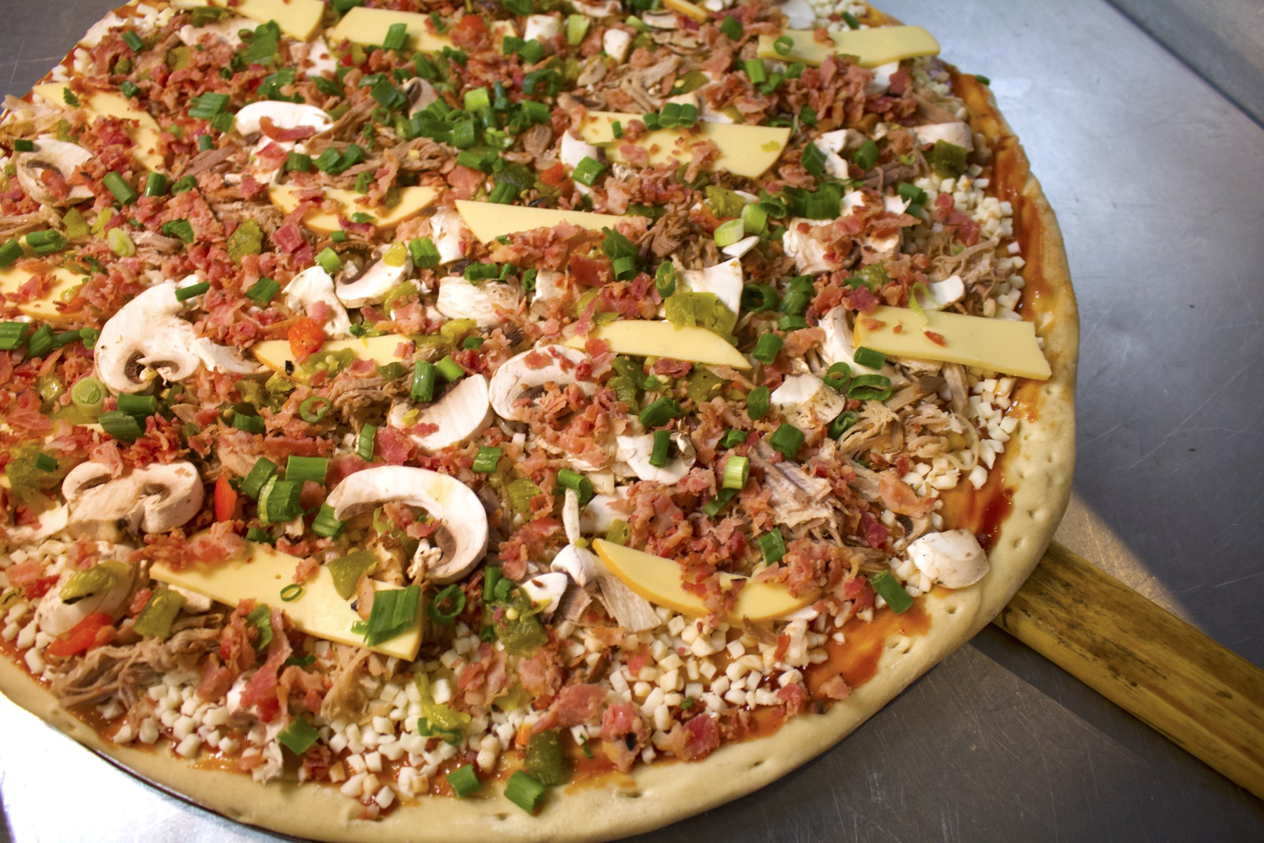 A loaded HomeSlice pizza fresh off the peel, ready to box up for Take & Bake